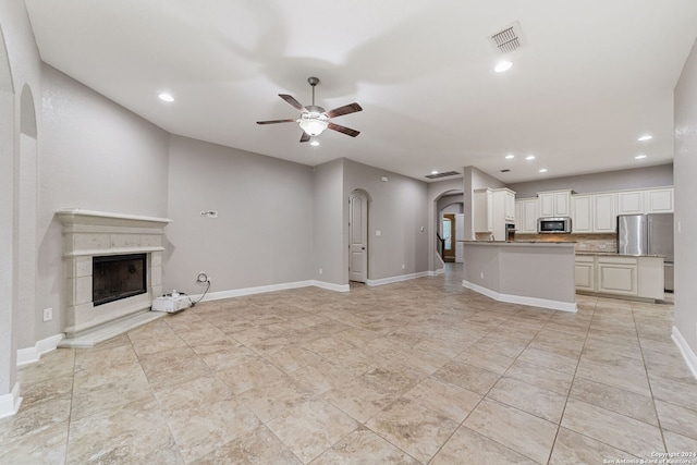 unfurnished living room with ceiling fan, a tile fireplace, and light tile floors