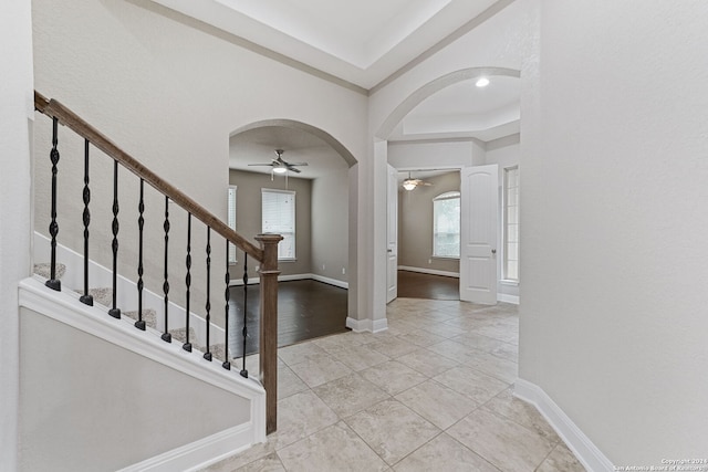 foyer with light hardwood / wood-style flooring, a wealth of natural light, ceiling fan, and a raised ceiling