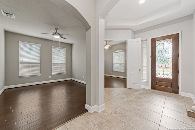 tiled foyer entrance with ceiling fan, a tray ceiling, and a textured ceiling