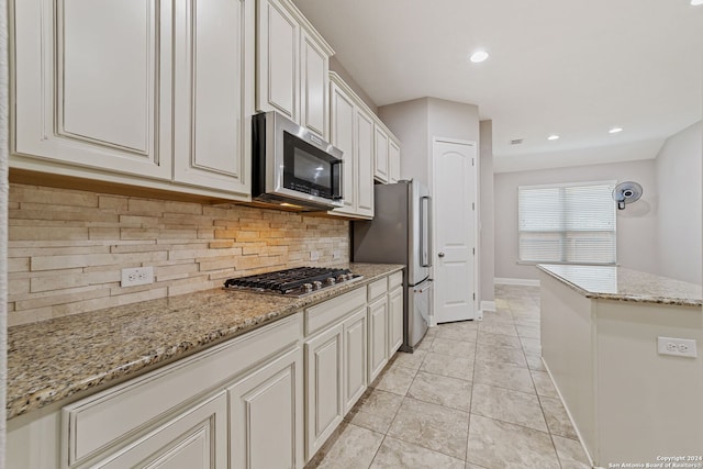 kitchen with light stone counters, light tile floors, backsplash, white cabinetry, and stainless steel appliances