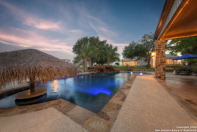 pool at dusk featuring a water slide and a patio area