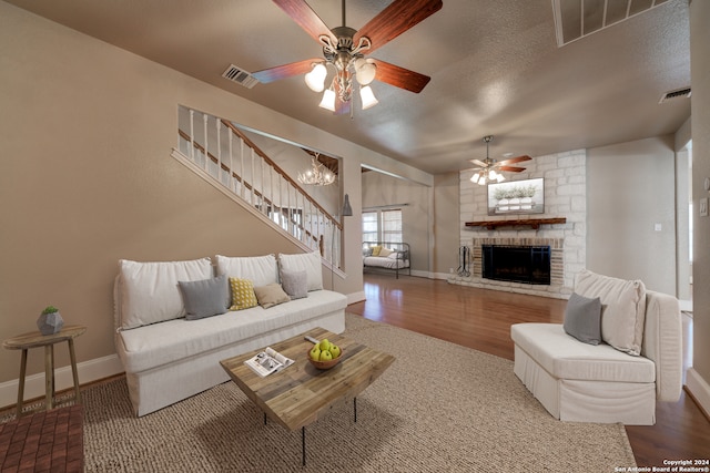 living room featuring ceiling fan with notable chandelier, wood-type flooring, a textured ceiling, and a fireplace