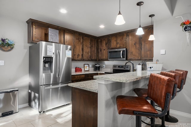 kitchen with dark brown cabinets, stainless steel appliances, decorative backsplash, light stone counters, and kitchen peninsula