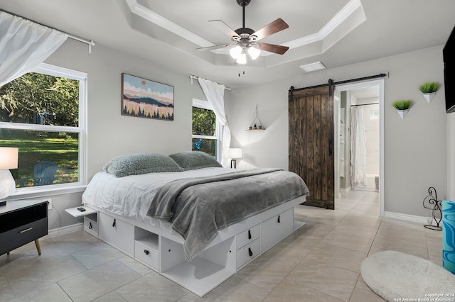 bedroom with light tile patterned floors, a barn door, ceiling fan, ensuite bathroom, and a raised ceiling