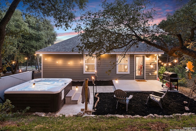 back house at dusk featuring a patio and a hot tub