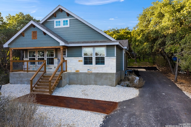 view of front of house with driveway, covered porch, a shingled roof, and stone siding