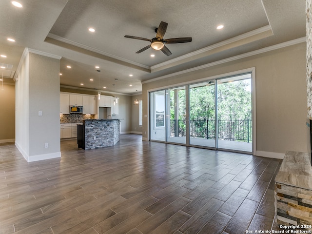 unfurnished living room with ceiling fan, a textured ceiling, a tray ceiling, dark wood-type flooring, and ornamental molding