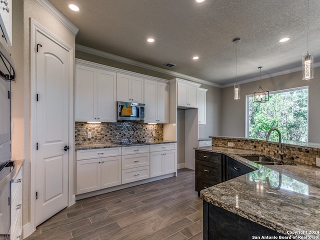 kitchen featuring light stone counters, sink, tasteful backsplash, hanging light fixtures, and ornamental molding