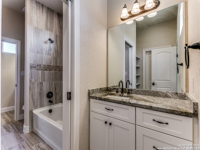 full bathroom featuring tiled shower / bath, vanity, hardwood / wood-style flooring, and toilet