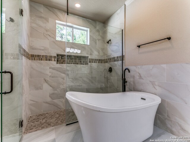 bathroom featuring independent shower and bath, tile flooring, tile walls, and a textured ceiling