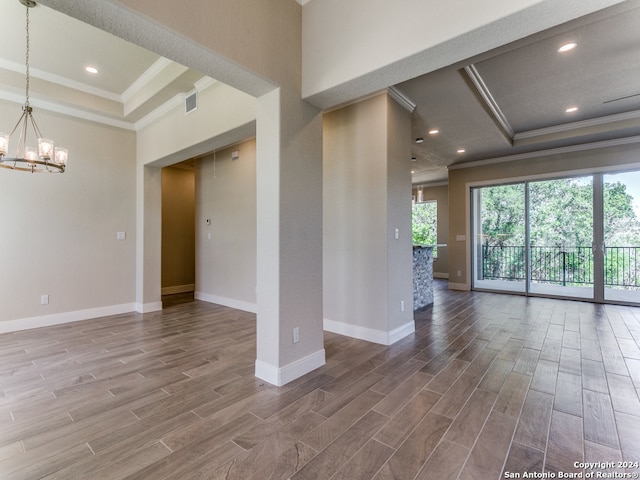 empty room with wood-type flooring, a tray ceiling, a chandelier, and crown molding