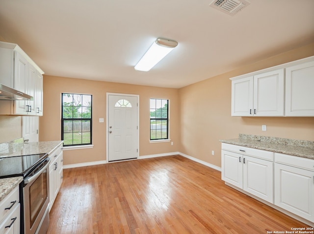 kitchen with light stone countertops, light wood-type flooring, stainless steel electric stove, and white cabinetry