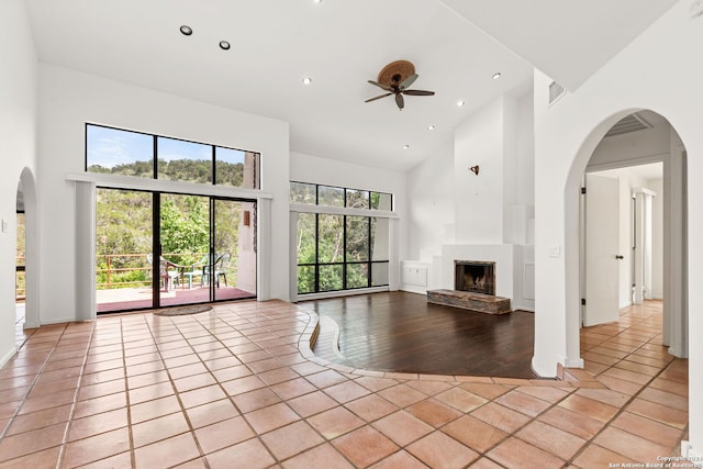 unfurnished living room featuring a towering ceiling, ceiling fan, a fireplace, and light tile patterned floors