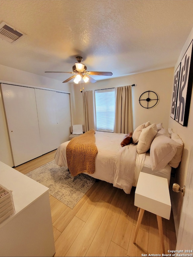 bedroom featuring a closet, light hardwood / wood-style flooring, ceiling fan, and a textured ceiling