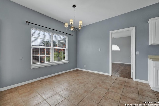 tiled spare room with an inviting chandelier