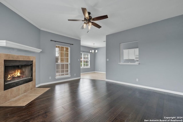 unfurnished living room featuring ceiling fan with notable chandelier, hardwood / wood-style floors, a tile fireplace, and crown molding