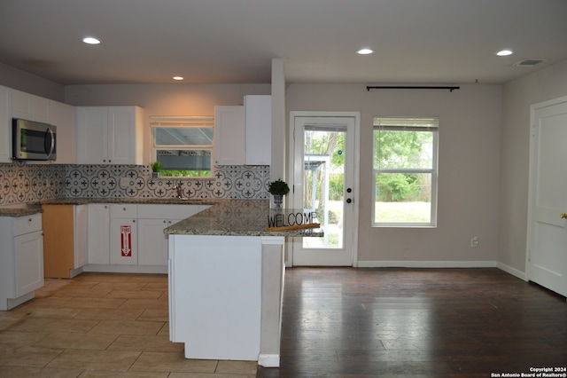 kitchen with white cabinets, hardwood / wood-style floors, backsplash, and light stone countertops