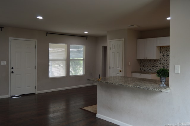 kitchen with white cabinets, dark hardwood / wood-style flooring, kitchen peninsula, and light stone counters