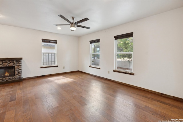 unfurnished living room featuring a stone fireplace, ceiling fan, and dark hardwood / wood-style floors