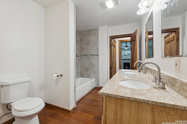 full bathroom with tiled shower / bath, dual vanity, toilet, and hardwood / wood-style floors