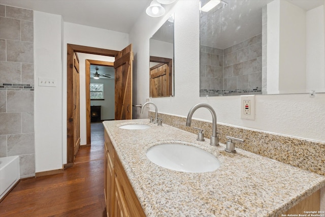 bathroom with double vanity, tiled shower / bath, wood-type flooring, and ceiling fan