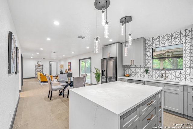 kitchen with decorative light fixtures, stainless steel appliances, sink, a center island, and light wood-type flooring