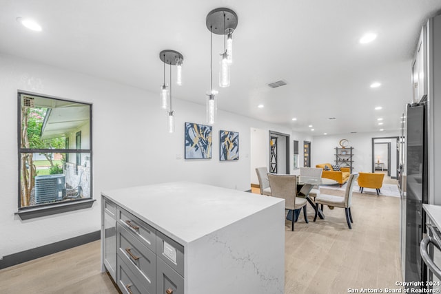 kitchen with hanging light fixtures, light wood-type flooring, gray cabinetry, light stone counters, and a kitchen island