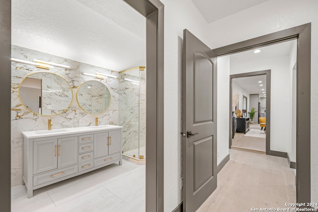 bathroom with tile walls, oversized vanity, a tile shower, hardwood / wood-style flooring, and double sink