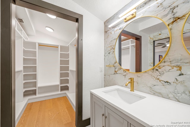 bathroom with wood-type flooring, tasteful backsplash, vaulted ceiling, and vanity