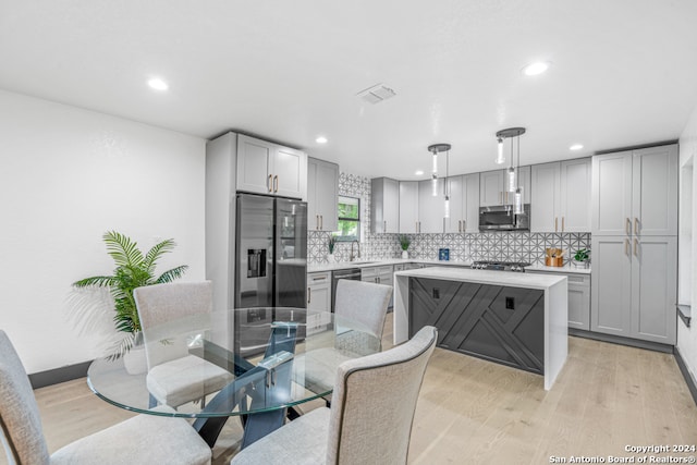 kitchen featuring appliances with stainless steel finishes, backsplash, light wood-type flooring, and decorative light fixtures