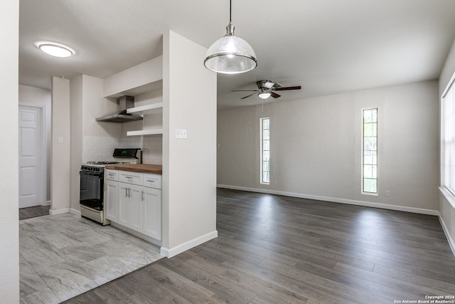 kitchen with butcher block countertops, backsplash, wall chimney range hood, range with gas stovetop, and light hardwood / wood-style flooring