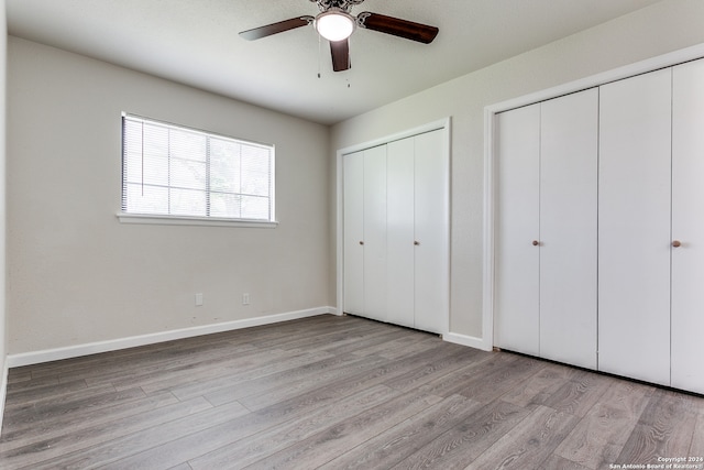 unfurnished bedroom featuring ceiling fan, light wood-type flooring, and two closets