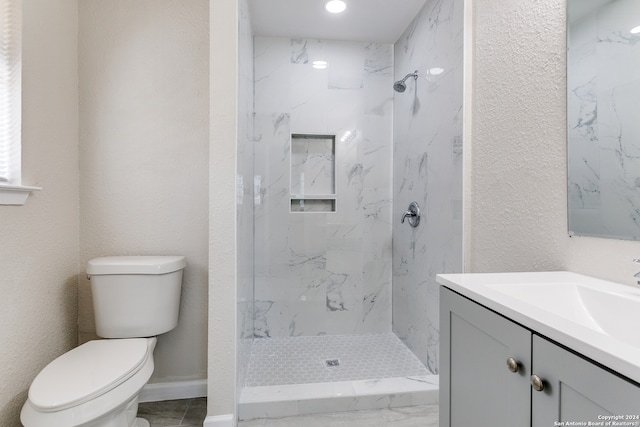 bathroom with toilet, tile floors, vanity, and a tile shower