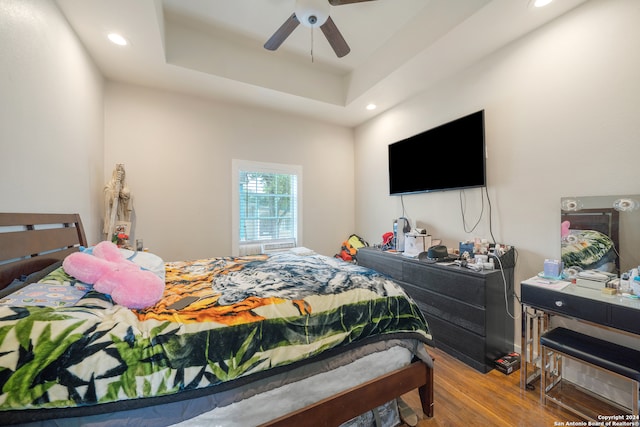 bedroom with hardwood / wood-style floors, ceiling fan, and a raised ceiling