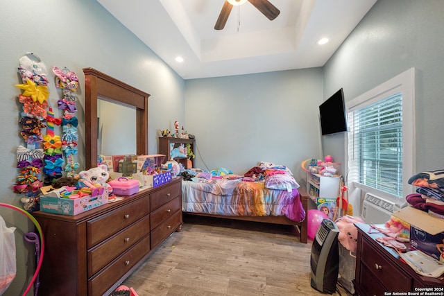 bedroom featuring ceiling fan, light wood-type flooring, and a tray ceiling