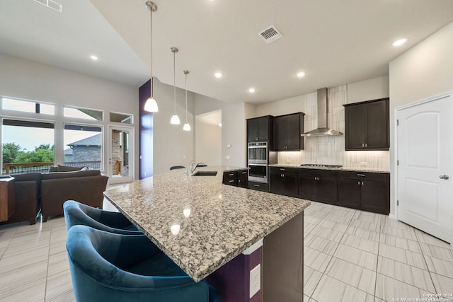 kitchen featuring backsplash, stainless steel appliances, a center island with sink, and wall chimney range hood