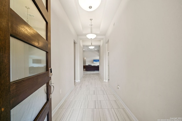 hall with a raised ceiling and tile floors