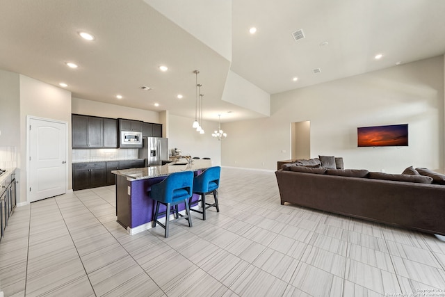 kitchen with appliances with stainless steel finishes, light tile floors, backsplash, a breakfast bar area, and a center island with sink