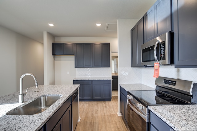 kitchen featuring backsplash, light hardwood / wood-style floors, stainless steel appliances, sink, and light stone counters