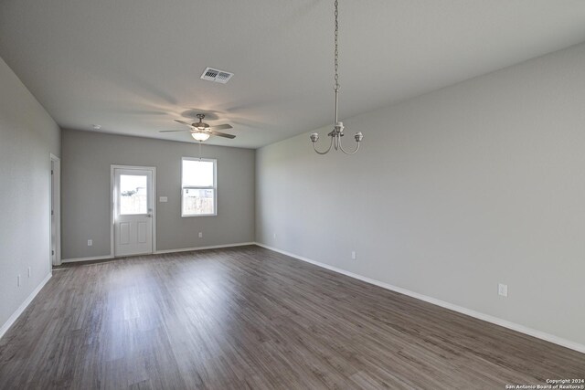 empty room featuring ceiling fan with notable chandelier and dark wood-type flooring