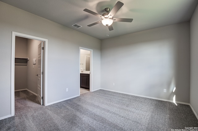 unfurnished bedroom with ceiling fan, a closet, a walk in closet, ensuite bathroom, and light colored carpet