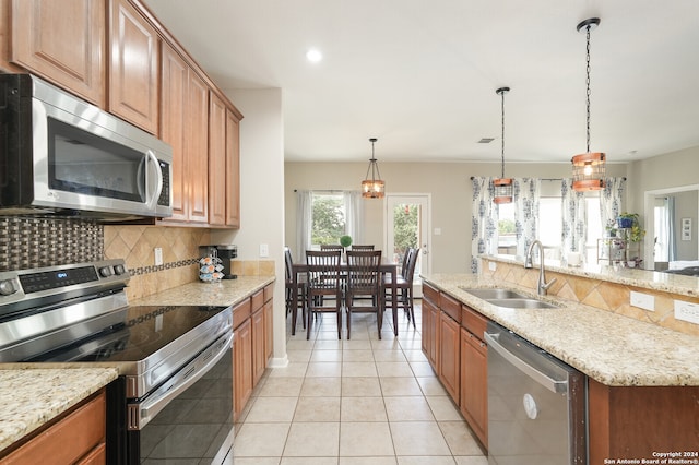 kitchen featuring light stone countertops, appliances with stainless steel finishes, hanging light fixtures, tasteful backsplash, and sink