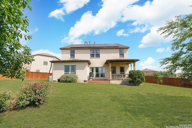 rear view of house featuring solar panels and a lawn