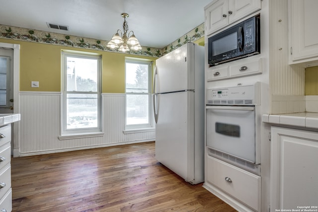 kitchen with hanging light fixtures, plenty of natural light, white appliances, and hardwood / wood-style flooring