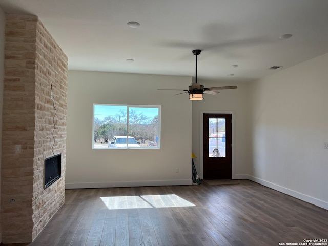 spare room featuring ceiling fan, dark hardwood / wood-style flooring, and a stone fireplace