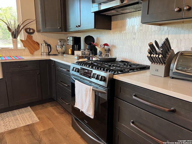 kitchen featuring fume extractor, light hardwood / wood-style floors, tasteful backsplash, gas range, and dark brown cabinetry