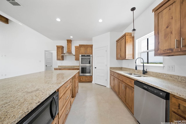 kitchen featuring wall chimney range hood, appliances with stainless steel finishes, light stone counters, decorative light fixtures, and sink