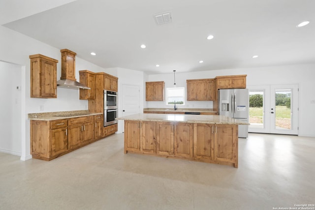 kitchen featuring decorative light fixtures, wall chimney range hood, a center island, light stone countertops, and appliances with stainless steel finishes