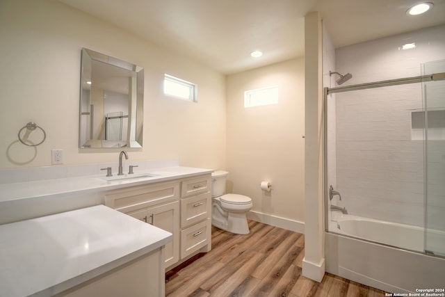 full bathroom with wood-type flooring, bath / shower combo with glass door, vanity, and toilet