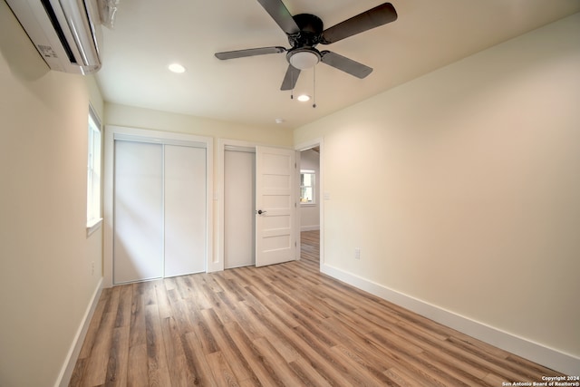 unfurnished bedroom featuring ceiling fan, light wood-type flooring, an AC wall unit, and multiple closets